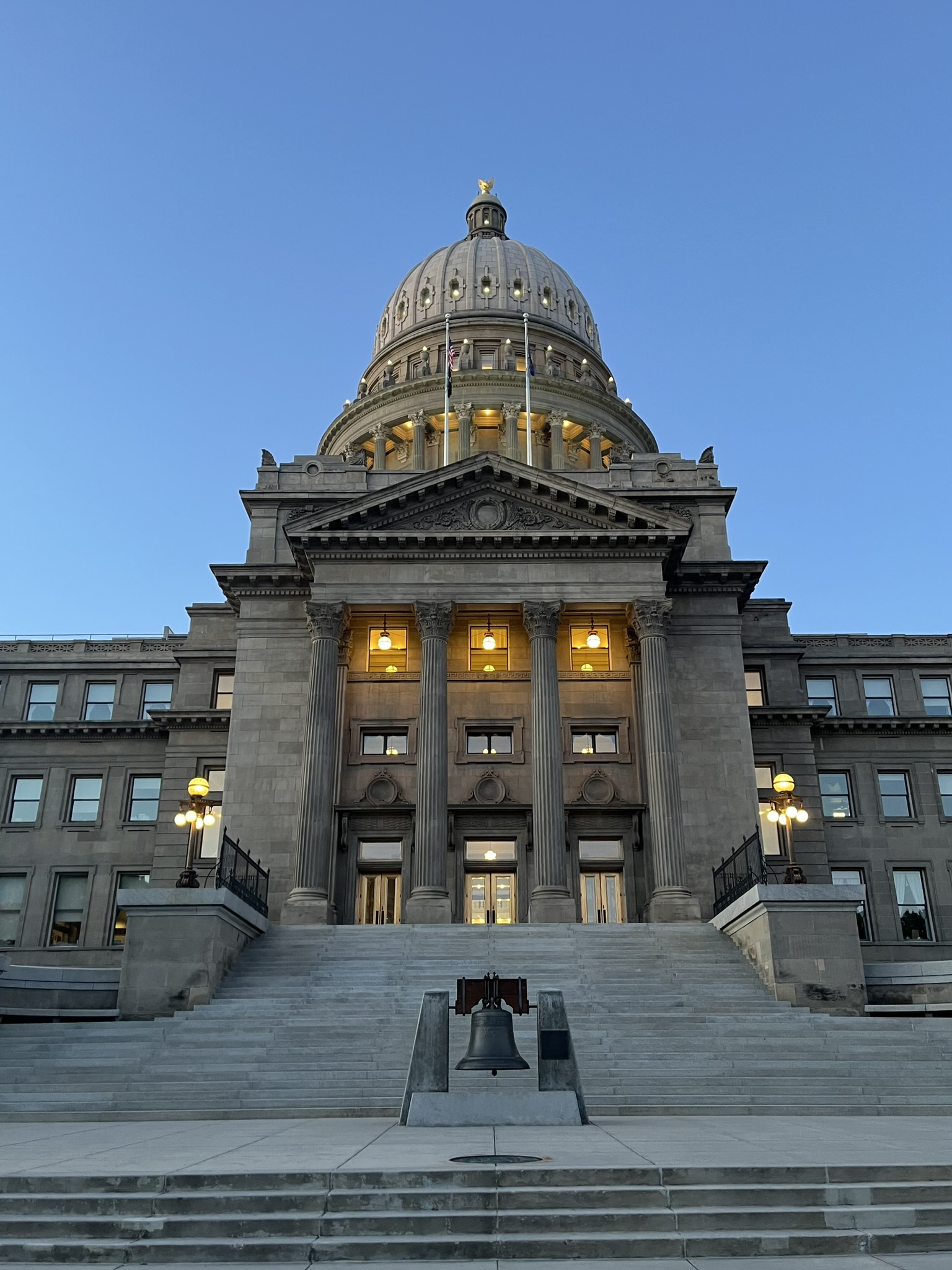 A large Capitol building with a small bell on stairs in front.